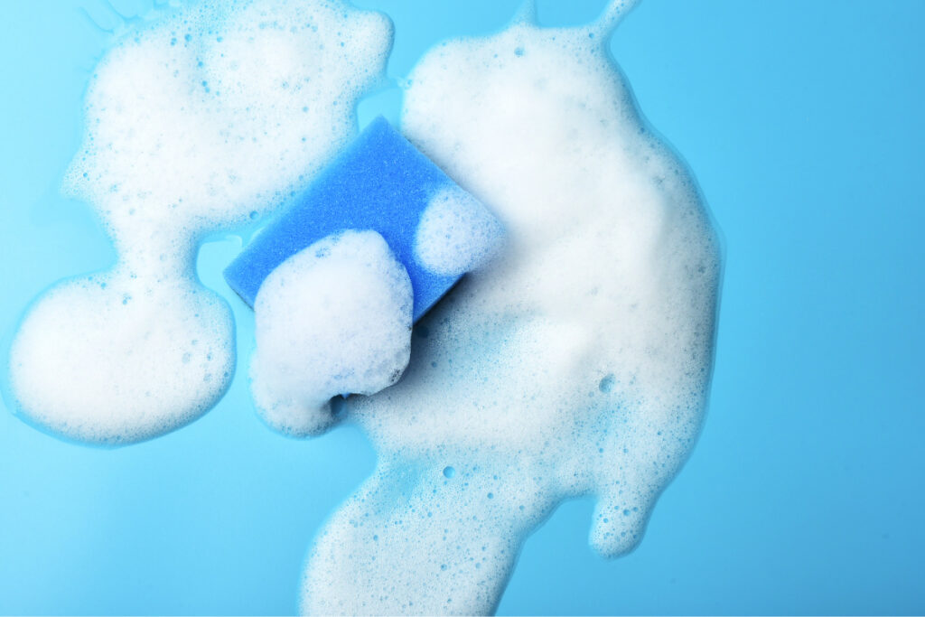 Fotografía cenital de esponja azul y mancha de espuma de jabón