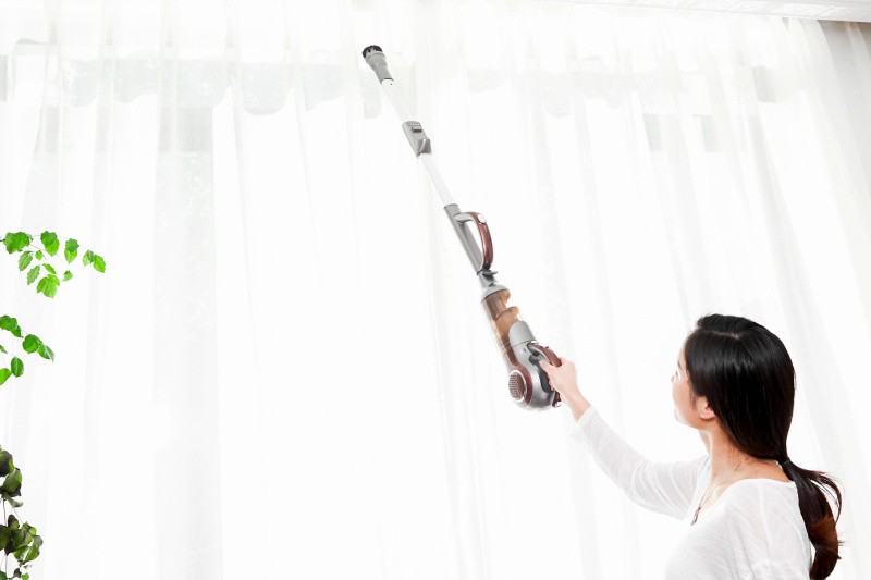 Mujer con aspiradora inalámbrica para limpiar cortinas rápidamente
