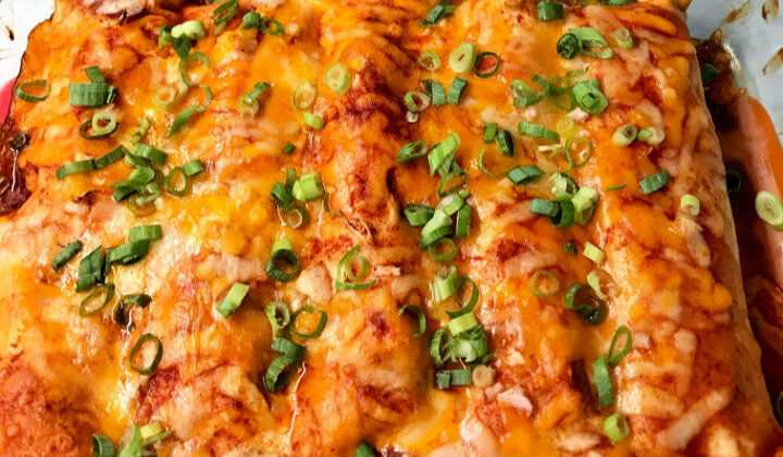 Sartén de enchiladas de pollo al horno cubiertas con una receta de salsa de enchilada casera, cebollas verdes en rodajas y queso rallado