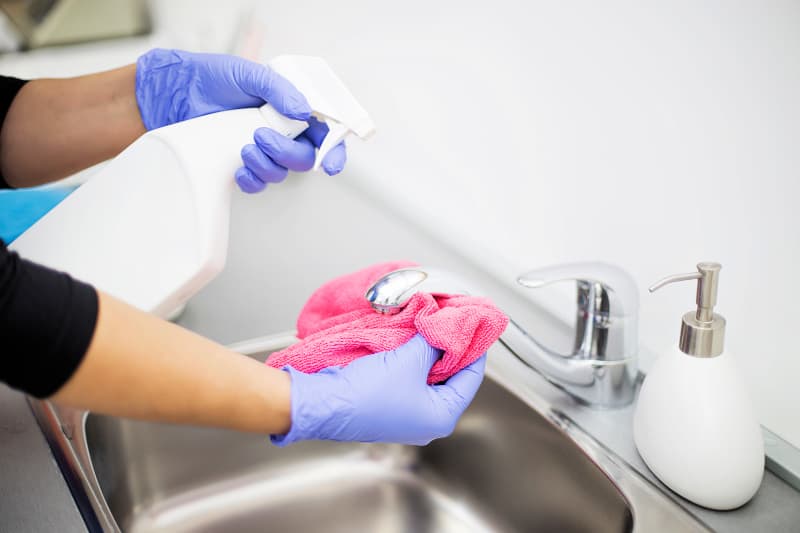 Mujer usando un desinfectante en aerosol en el grifo y las manijas de la cocina