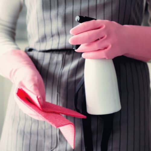 Mujer con guantes de goma y sosteniendo una botella de spray desinfectante casero